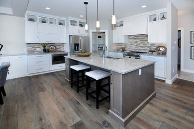 Mid-sized transitional l-shaped medium tone wood floor and brown floor eat-in kitchen photo in Calgary with a double-bowl sink, recessed-panel cabinets, white cabinets, granite countertops, multicolored backsplash, glass tile backsplash, stainless steel appliances and an island