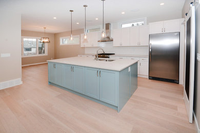 Large trendy l-shaped light wood floor and beige floor open concept kitchen photo in Calgary with an undermount sink, shaker cabinets, white cabinets, granite countertops, white backsplash, subway tile backsplash, stainless steel appliances and an island