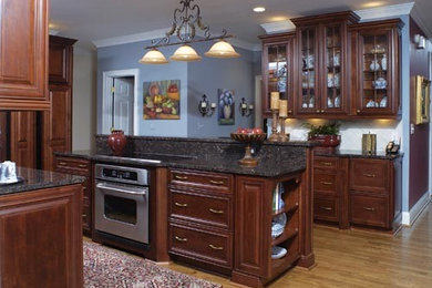 Example of a large classic l-shaped medium tone wood floor eat-in kitchen design in Atlanta with an undermount sink, recessed-panel cabinets, dark wood cabinets, granite countertops, beige backsplash, stone tile backsplash, stainless steel appliances and an island