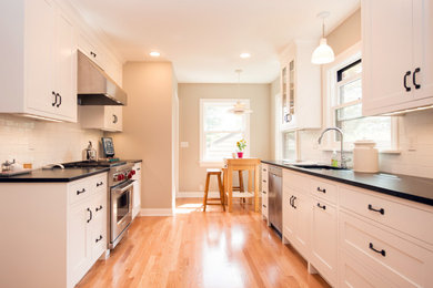 Enclosed kitchen - mid-sized traditional galley light wood floor and beige floor enclosed kitchen idea in Seattle with an undermount sink, shaker cabinets, white cabinets, granite countertops, white backsplash, subway tile backsplash, stainless steel appliances, no island and black countertops