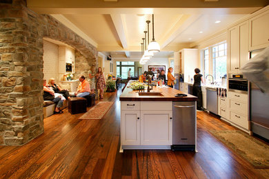 Example of a large arts and crafts u-shaped dark wood floor and brown floor eat-in kitchen design in Seattle with a drop-in sink, recessed-panel cabinets, white cabinets, wood countertops, stainless steel appliances and an island