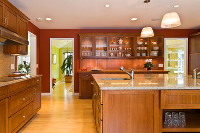 This is an example of a large contemporary l-shaped kitchen/diner in Minneapolis with a submerged sink, shaker cabinets, medium wood cabinets, engineered stone countertops, multi-coloured splashback, stone slab splashback, stainless steel appliances, light hardwood flooring and an island.