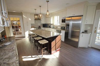 Example of a mid-sized transitional l-shaped light wood floor eat-in kitchen design in Providence with an undermount sink, shaker cabinets, white cabinets, granite countertops, white backsplash, ceramic backsplash, stainless steel appliances and an island
