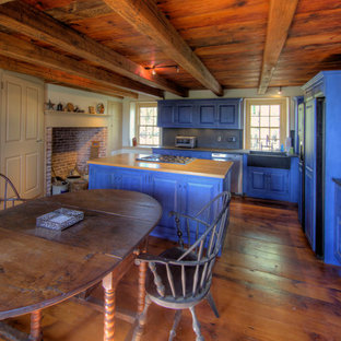 Design ideas for a mid-sized country l-shaped eat-in kitchen in Philadelphia with raised-panel cabinets, blue cabinets, a farmhouse sink, wood benchtops, blue splashback, panelled appliances, dark hardwood floors, with island and slate splashback.