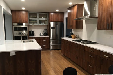 Large galley kitchen/diner in Baltimore with a submerged sink, flat-panel cabinets, brown cabinets, engineered stone countertops, white splashback, ceramic splashback, stainless steel appliances, light hardwood flooring, an island, brown floors and white worktops.