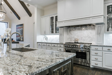 Open concept kitchen - transitional l-shaped medium tone wood floor open concept kitchen idea in Dallas with an undermount sink, raised-panel cabinets, gray cabinets, granite countertops, gray backsplash, stone tile backsplash, stainless steel appliances and an island