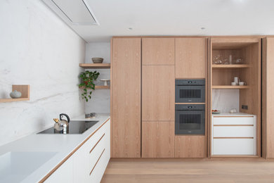 Design ideas for a medium sized modern l-shaped kitchen in London with an integrated sink, flat-panel cabinets, light wood cabinets, white splashback, black appliances, light hardwood flooring, no island, beige floors and white worktops.