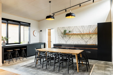 На фото: угловая кухня в современном стиле с обеденным столом, плоскими фасадами, черными фасадами, бетонным полом, серым полом и черной столешницей без острова с