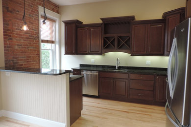 Example of a mid-sized classic l-shaped light wood floor kitchen design in Grand Rapids with raised-panel cabinets, dark wood cabinets, stainless steel appliances, a peninsula and an undermount sink