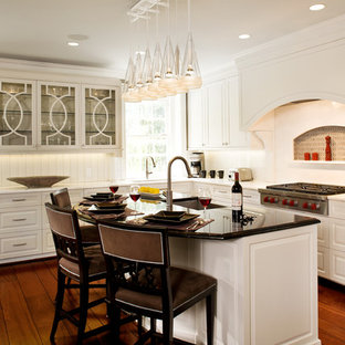 Inspiration pour une grand cuisine ouverte traditionnelle en L avec un placard avec porte à panneau surélevé, des portes de placard blanches, un évier encastré, un plan de travail en quartz modifié, une crédence blanche, une crédence en bois, un électroménager encastrable, un sol en bois foncé, un îlot central et un sol marron.