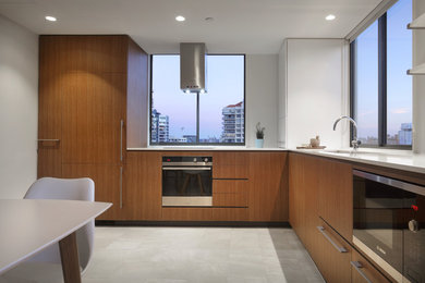 Modern inredning av ett kök, med en undermonterad diskho, skåp i mellenmörkt trä, bänkskiva i kvarts, svarta vitvaror och klinkergolv i porslin