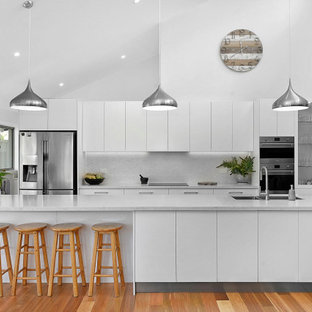Inspiration for a contemporary galley kitchen in Sydney with an undermount sink, flat-panel cabinets, white cabinets, grey splashback, stainless steel appliances, medium hardwood floors, with island, brown floor, grey benchtop and vaulted.