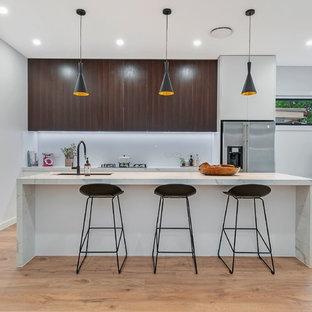 Inspiration for a contemporary l-shaped kitchen in Sydney with an undermount sink, flat-panel cabinets, white cabinets, stainless steel appliances, medium hardwood floors, with island, brown floor and white benchtop.