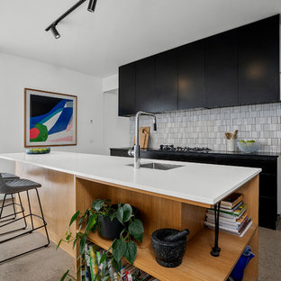 This is an example of a contemporary open plan kitchen in Geelong with a drop-in sink, black cabinets, quartz benchtops, white splashback, porcelain splashback, concrete floors, with island, grey floor and multi-coloured benchtop.