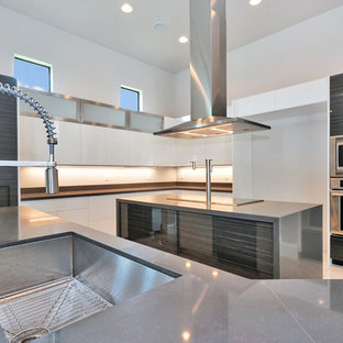 Photo of a large contemporary l-shaped open plan kitchen in Miami with an undermount sink, flat-panel cabinets, white cabinets, concrete benchtops, beige splashback, stainless steel appliances, marble floors, multiple islands and white floor.