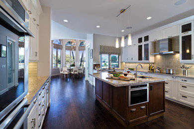 Large transitional galley dark wood floor eat-in kitchen photo in Miami with a drop-in sink, recessed-panel cabinets, white cabinets, granite countertops, gray backsplash, glass tile backsplash, stainless steel appliances and an island