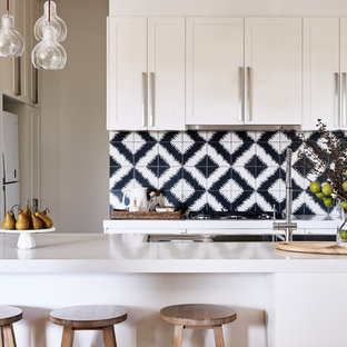 This is an example of a transitional l-shaped kitchen in Melbourne with a double-bowl sink, shaker cabinets, white cabinets, quartz benchtops, cement tile splashback, stainless steel appliances, light hardwood floors, with island, white benchtop and black splashback.