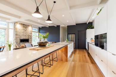 Zweizeilige Moderne Küche mit Unterbauwaschbecken, flächenbündigen Schrankfronten, weißen Schränken, schwarzen Elektrogeräten, braunem Holzboden, Kücheninsel und braunem Boden in Melbourne