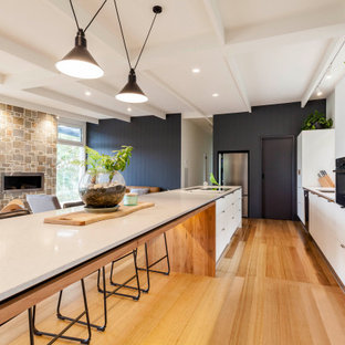 Photo of a contemporary galley kitchen in Melbourne with an undermount sink, flat-panel cabinets, white cabinets, black appliances, medium hardwood floors, with island and brown floor.