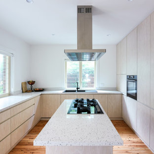 Inspiration for a large contemporary u-shaped separate kitchen in Sydney with a drop-in sink, flat-panel cabinets, light wood cabinets, quartz benchtops, beige splashback, engineered quartz splashback, black appliances, medium hardwood floors, with island, brown floor and beige benchtop.