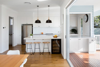 Exempel på ett mellanstort modernt vit vitt kök, med vita skåp, stänkskydd i cementkakel, rostfria vitvaror, mellanmörkt trägolv, en köksö, en nedsänkt diskho, bänkskiva i kvarts, vitt stänkskydd och brunt golv