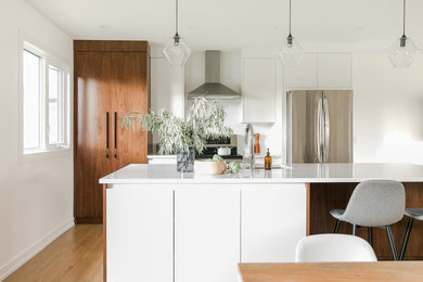 Mittelgroße Moderne Küche mit flächenbündigen Schrankfronten, hellbraunen Holzschränken, Quarzwerkstein-Arbeitsplatte, Küchenrückwand in Weiß, Kücheninsel und weißer Arbeitsplatte in Calgary