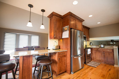 Mid-sized elegant l-shaped medium tone wood floor and brown floor open concept kitchen photo in Omaha with shaker cabinets, medium tone wood cabinets, granite countertops, stainless steel appliances and a peninsula