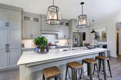 Inspiration for a transitional galley medium tone wood floor kitchen remodel in Toronto with a double-bowl sink, recessed-panel cabinets, gray cabinets, marble countertops, white backsplash, stainless steel appliances and an island