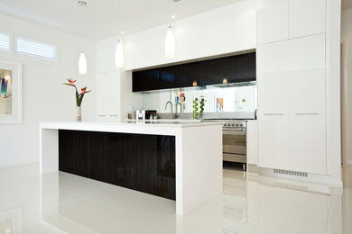 Modern inredning av ett mellanstort kök, med en undermonterad diskho, släta luckor, vita skåp, bänkskiva i kvarts, spegel som stänkskydd, rostfria vitvaror, klinkergolv i porslin och en köksö