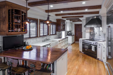 Example of a large farmhouse galley light wood floor and brown floor kitchen pantry design in San Diego with a farmhouse sink, flat-panel cabinets, dark wood cabinets, wood countertops, stone tile backsplash, black appliances, a peninsula and gray backsplash