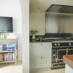 Design ideas for a mid-sized contemporary galley eat-in kitchen in London with an integrated sink, raised-panel cabinets, green cabinets, stainless steel appliances, limestone floors, with island, granite benchtops, metallic splashback, white floor and black benchtop.