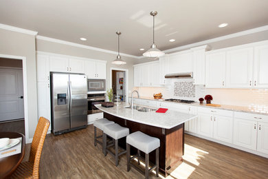Inspiration for a large timeless l-shaped vinyl floor eat-in kitchen remodel in Milwaukee with a double-bowl sink, raised-panel cabinets, white cabinets, quartz countertops, white backsplash, subway tile backsplash, stainless steel appliances and an island