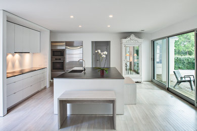 Eat-in kitchen - large modern bamboo floor eat-in kitchen idea in Austin with an integrated sink, flat-panel cabinets, white cabinets, stainless steel countertops, white backsplash, ceramic backsplash, stainless steel appliances and an island