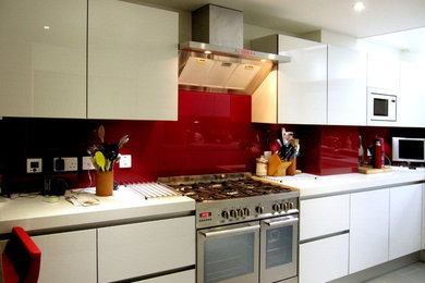 Inspiration for a large modern u-shaped enclosed kitchen in London with a double-bowl sink, flat-panel cabinets, white cabinets, quartz worktops, red splashback, glass sheet splashback, stainless steel appliances, porcelain flooring and a breakfast bar.