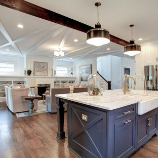 Photo of a mid-sized arts and crafts single-wall open plan kitchen in Atlanta with a farmhouse sink, glass-front cabinets, white cabinets, marble benchtops, white splashback, marble splashback, stainless steel appliances, medium hardwood floors, with island and beige floor.