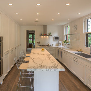 Example of a large transitional u-shaped dark wood floor enclosed kitchen design in Minneapolis with an undermount sink, shaker cabinets, white cabinets, marble countertops, white backsplash, porcelain backsplash, stainless steel appliances and an island