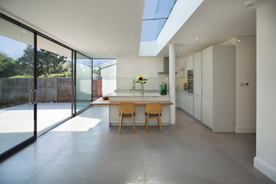 Große Moderne Küche in L-Form mit flächenbündigen Schrankfronten, weißen Schränken, Glasrückwand, Küchengeräten aus Edelstahl, Halbinsel und grauem Boden in London