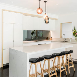 Contemporary l-shaped kitchen in Melbourne with an undermount sink, flat-panel cabinets, white cabinets, metallic splashback, mirror splashback, panelled appliances, painted wood floors, with island, black floor and white benchtop.