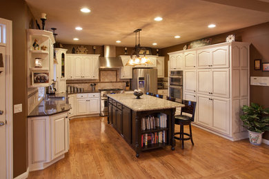 Example of a large classic u-shaped light wood floor eat-in kitchen design in St Louis with an undermount sink, recessed-panel cabinets, white cabinets, granite countertops, beige backsplash, ceramic backsplash, stainless steel appliances and an island