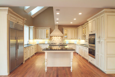 Example of a large classic u-shaped medium tone wood floor enclosed kitchen design in Chicago with an undermount sink, raised-panel cabinets, white cabinets, stainless steel appliances and an island