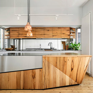 Design ideas for a contemporary l-shaped kitchen in Melbourne with an undermount sink, flat-panel cabinets, medium wood cabinets, mirror splashback, black appliances, light hardwood floors, with island and multi-coloured benchtop.