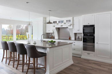 Photo of a large classic single-wall open plan kitchen in Other with an integrated sink, beaded cabinets, white cabinets, quartz worktops, brown splashback, stone slab splashback, stainless steel appliances, medium hardwood flooring, an island and brown floors.