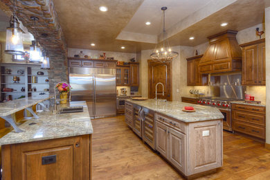 Example of a large tuscan medium tone wood floor kitchen design in Denver with an undermount sink, raised-panel cabinets, medium tone wood cabinets, granite countertops, beige backsplash, stone tile backsplash, stainless steel appliances and two islands