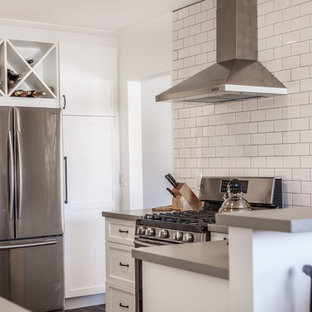 Inspiration for a mid-sized contemporary u-shaped separate kitchen in Orange County with a farmhouse sink, shaker cabinets, white cabinets, concrete benchtops, white splashback, subway tile splashback, stainless steel appliances, laminate floors, a peninsula, black floor and grey benchtop.