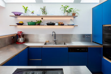 Küche in U-Form mit Einbauwaschbecken, flächenbündigen Schrankfronten, blauen Schränken, Edelstahl-Arbeitsplatte, Küchenrückwand in Metallic und Elektrogeräten mit Frontblende in London