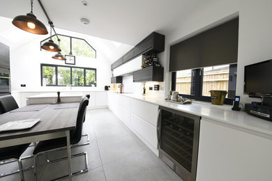 This is an example of a large modern u-shaped kitchen/diner in Kent with a built-in sink, flat-panel cabinets, white cabinets, composite countertops, white splashback, integrated appliances, porcelain flooring, an island and grey floors.