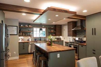 デンバーにある広いラスティックスタイルのおしゃれなキッチン (エプロンフロントシンク、フラットパネル扉のキャビネット、緑のキャビネット、木材カウンター、グレーのキッチンパネル、サブウェイタイルのキッチンパネル、シルバーの調理設備、無垢フローリング、茶色い床、茶色いキッチンカウンター、表し梁) の写真