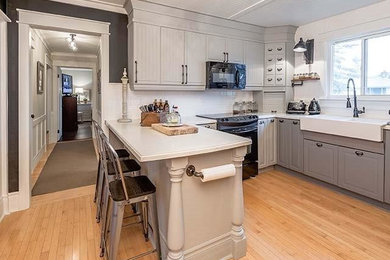 Inspiration for a mid-sized cottage u-shaped light wood floor and brown floor kitchen remodel in Toronto with a farmhouse sink, raised-panel cabinets, gray cabinets, marble countertops, white backsplash, subway tile backsplash, black appliances and a peninsula