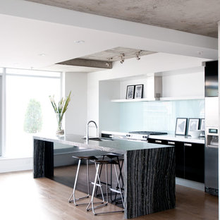 Ispirazione per una cucina moderna di medie dimensioni con elettrodomestici in acciaio inossidabile, lavello sottopiano, ante lisce, ante nere, paraspruzzi bianco, paraspruzzi in lastra di pietra, parquet chiaro, isola e pavimento beige