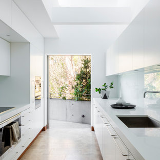 This is an example of a large midcentury galley separate kitchen in Sydney with an undermount sink, quartz benchtops, white splashback, glass sheet splashback, black appliances, travertine floors, white benchtop, flat-panel cabinets, white cabinets, no island and beige floor.